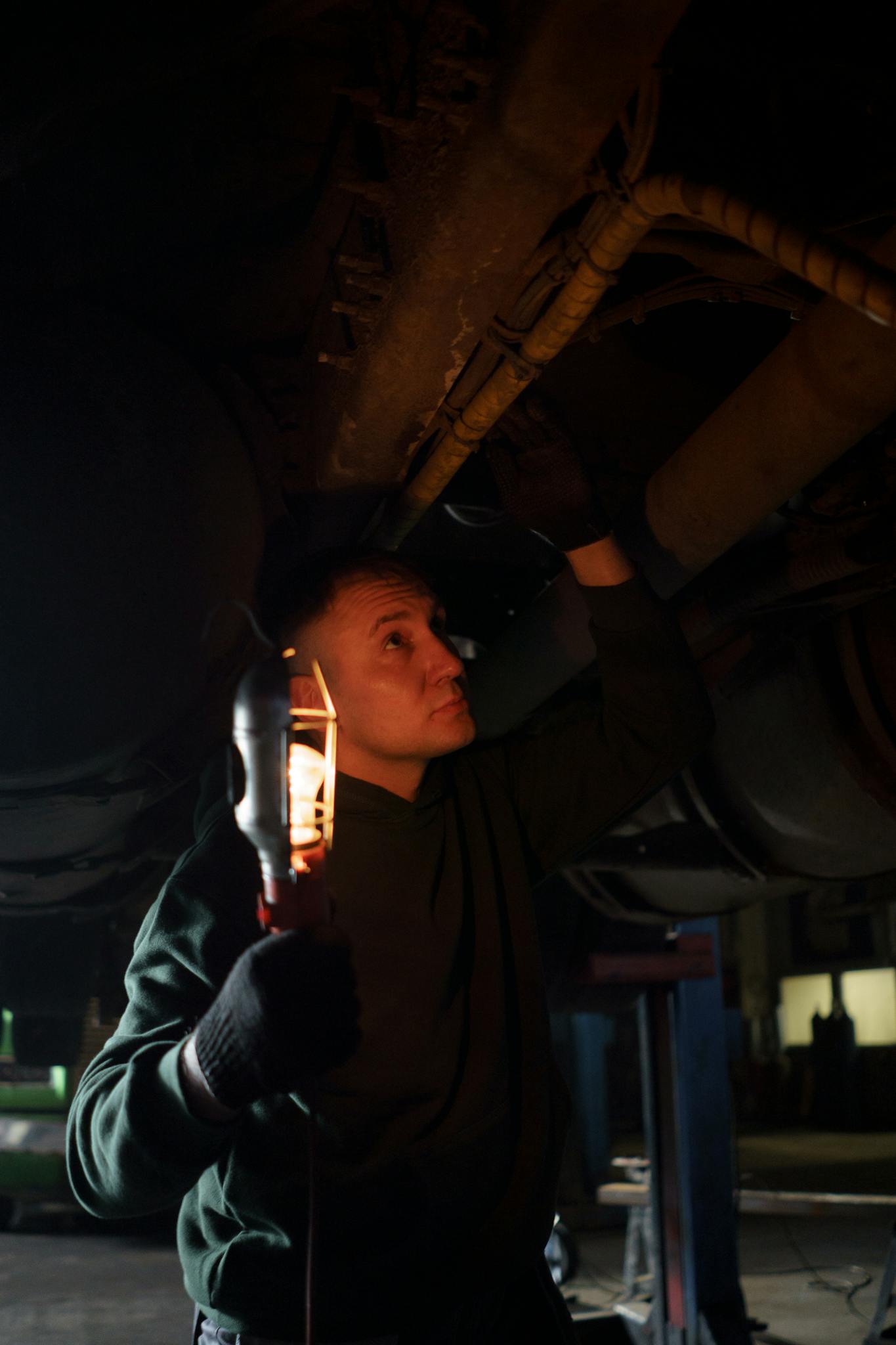 Automotive mechanic using handheld light to inspect a vehicle's underbody in a repair shop.